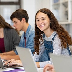 Teen girl smiling while working on laptop at school
