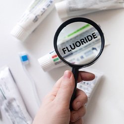 Hand holding magnifying glass zoomed in on “fluoride” on toothpaste tube
