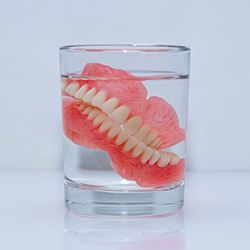 Dentures soaking in glass with clear liquid