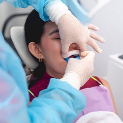 Dentist placing two foam fluoride trays into girl’s mouth