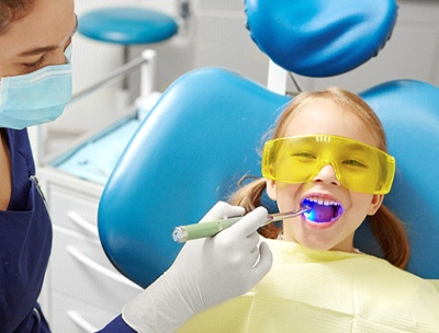 A dental hygienist uses a curing light to harden dental sealants placed on a little girl’s back teeth