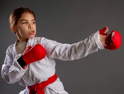 A little girl wearing a boxing robe and gloves wears a customized mouthguard to protect her smile