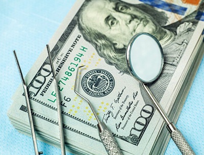 dental instruments lying on top of a stack of hundred-dollar bills