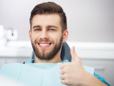 smiling man in dental chair giving thumbs up