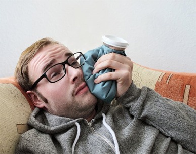 man lying on couch holding cold compress to his cheek
