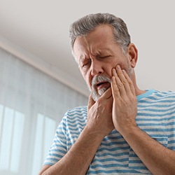 An older man holds his mouth while experiencing some discomfort after having dental implants placed in Toledo