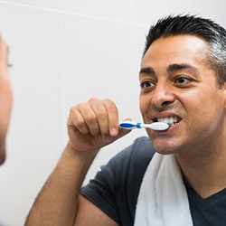 A man gently brushes his teeth after having dental implants surgically placed in Toledo