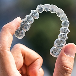 Hand holding up Invisalign aligner outside 