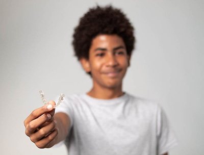 Teen smiling while holding Invisalign aligner