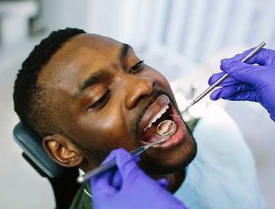 Blue-gloved hands examining man’s mouth