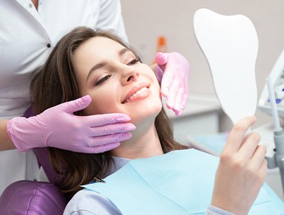 Woman in dental chair smiling at reflection in handheld mirror