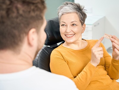 Woman in dental chair holding dentures and pointing to them