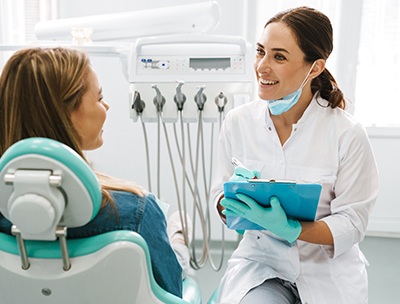 Smiling dentist talking to patient and taking notes on clipboard