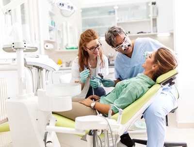 A female patient in the dentist’s chair while the dentist and dental assistant examine her mouth