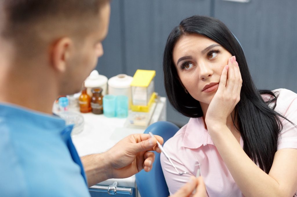 Woman experiencing tooth pain and talking to her dentist.