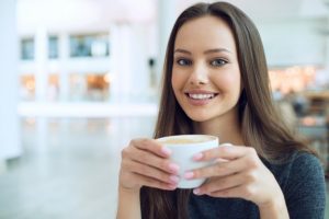 Mulher sorrindo e tomando café.