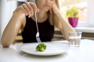 Woman eating one piece of broccoli on her plate and a glass of water.